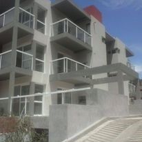 Edificio de apartamentos moderno de color blanco con balcones y una escalera exterior bajo un cielo azul.