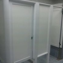 Puertas blancas de los cubículos de un baño público en un pasillo alicatado.