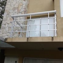 Balcón con barandilla blanca y puerta de cristal en una fachada de edificio de piedra y color beige.