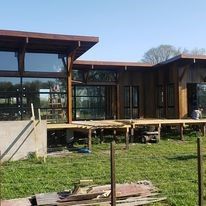 Exterior de una casa moderna con grandes ventanales y una terraza de madera elevada en un jardín con césped.