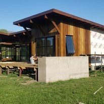 Cabaña moderna de madera con porche de hormigón bajo un cielo azul, en un césped.