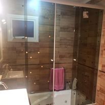 Ducha de cristal con paredes revestidas de azulejos que imitan la madera, toallero para colgar en el interior.