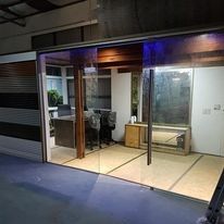 Interior de una tienda con fachada de cristal, con zona de exposición vacía, sillas y banco por la noche.