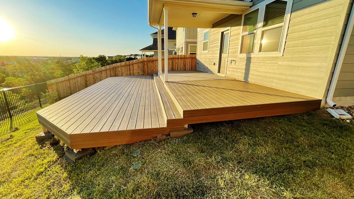A multi-level wooden deck attached to the back of a house, featuring light and dark wood finishes at sunset.
