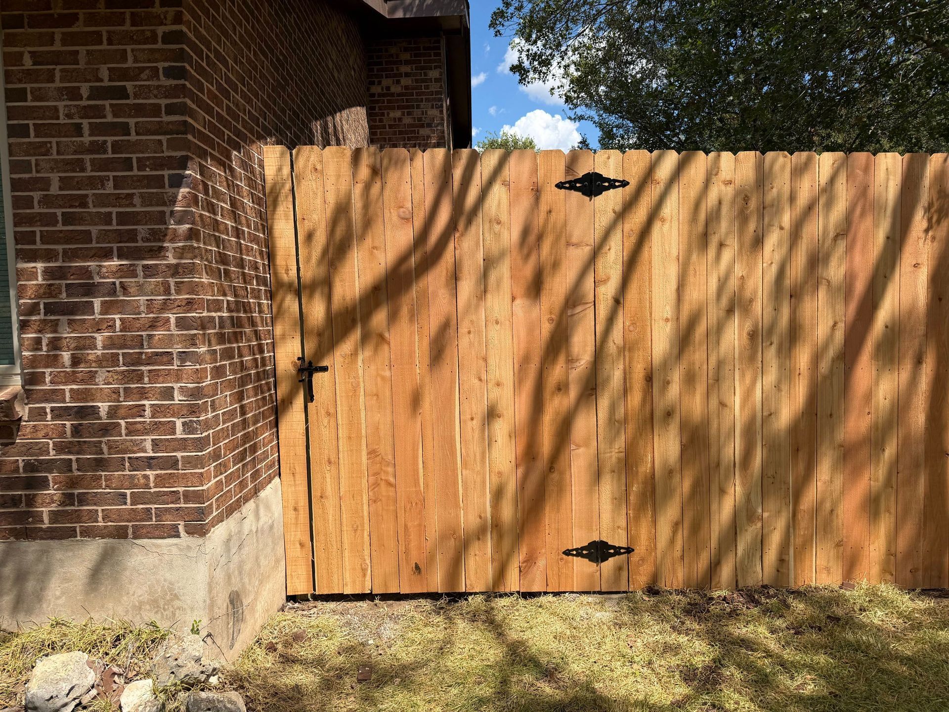 Wooden gate beside a brick house and concrete wall in a grassy yard.