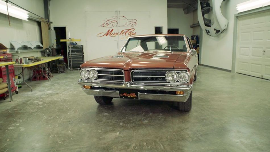 Brown classic Pontiac car inside a garage, parked in front of the open door.