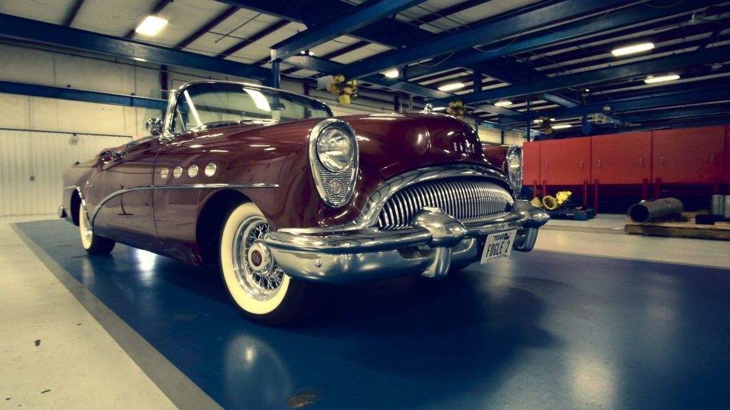 Red classic convertible car parked inside a warehouse.