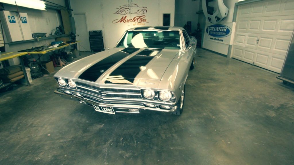 Silver classic car with black racing stripes parked inside a garage.