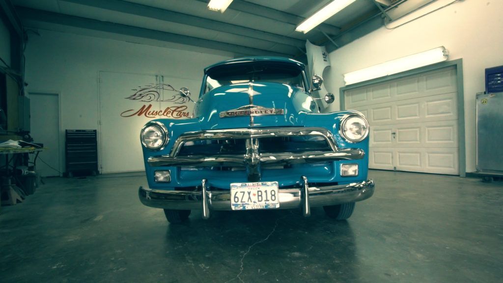 Blue classic truck parked in a garage with a closed white garage door.