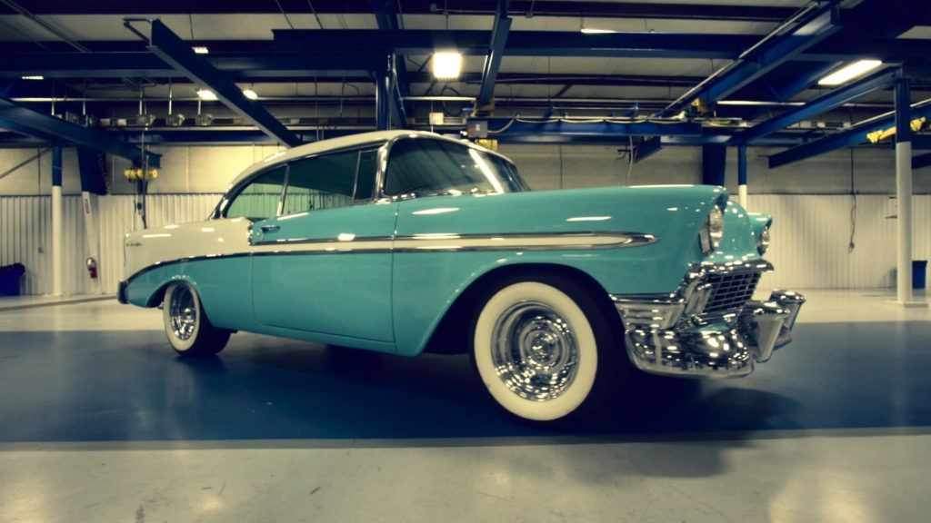 Blue and white classic car with whitewall tires, parked in an indoor garage.