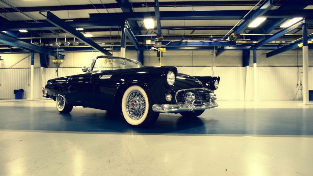 Black vintage convertible car with white-wall tires parked inside a large garage.