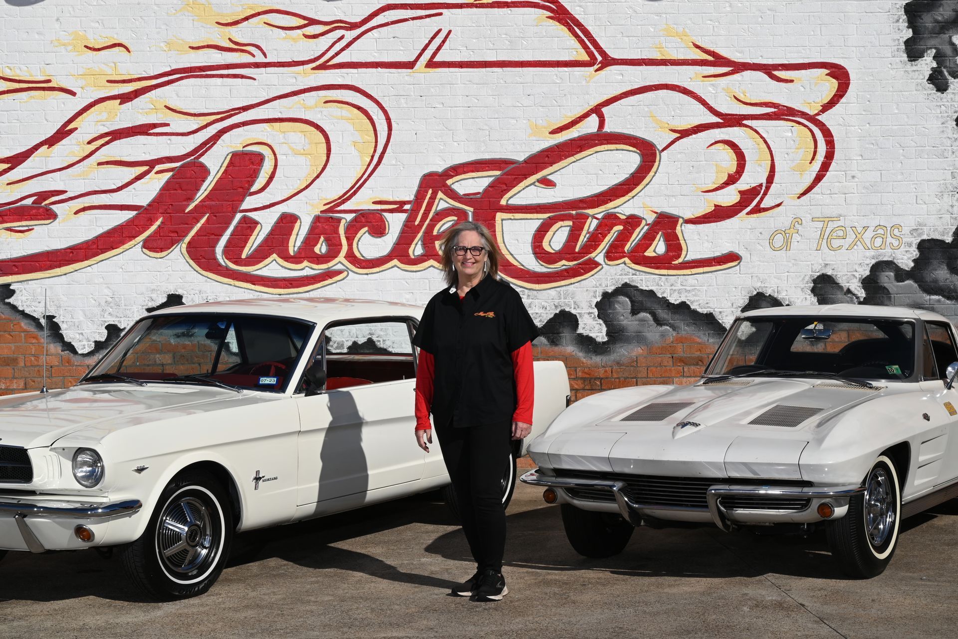 Man standing between two white classic muscle cars in front of a 