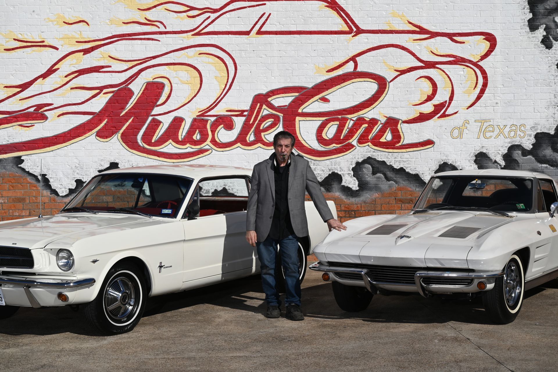 Man standing between two white classic muscle cars in front of a 