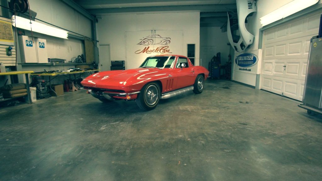 Red vintage Corvette in a garage with tools and a white door.