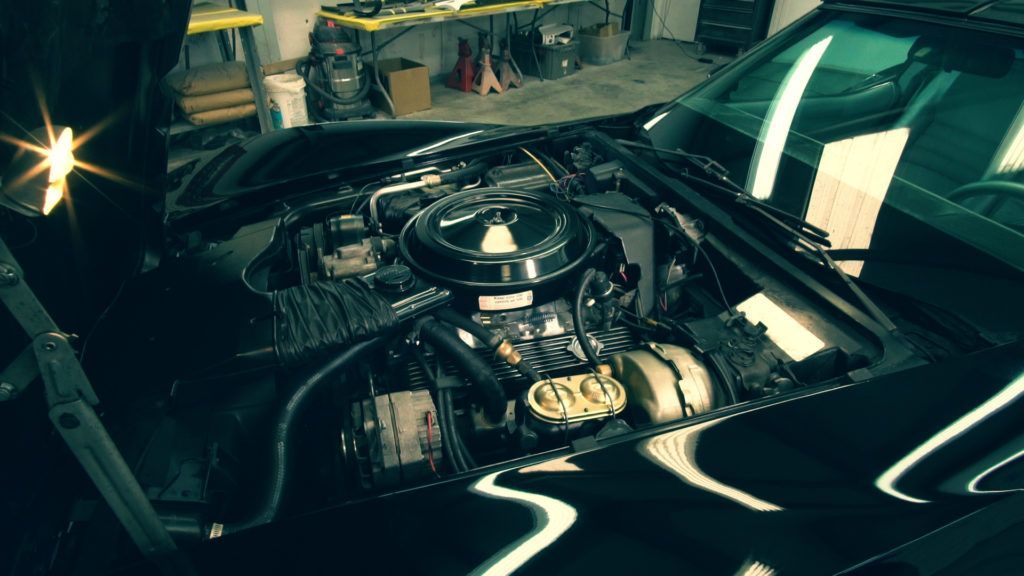 Black Corvette with hood up, engine visible in a garage.