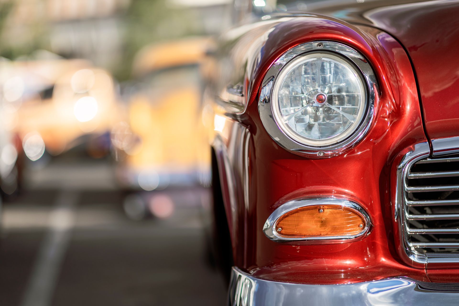 Red classic car headlight and fender, chrome details, close-up view.