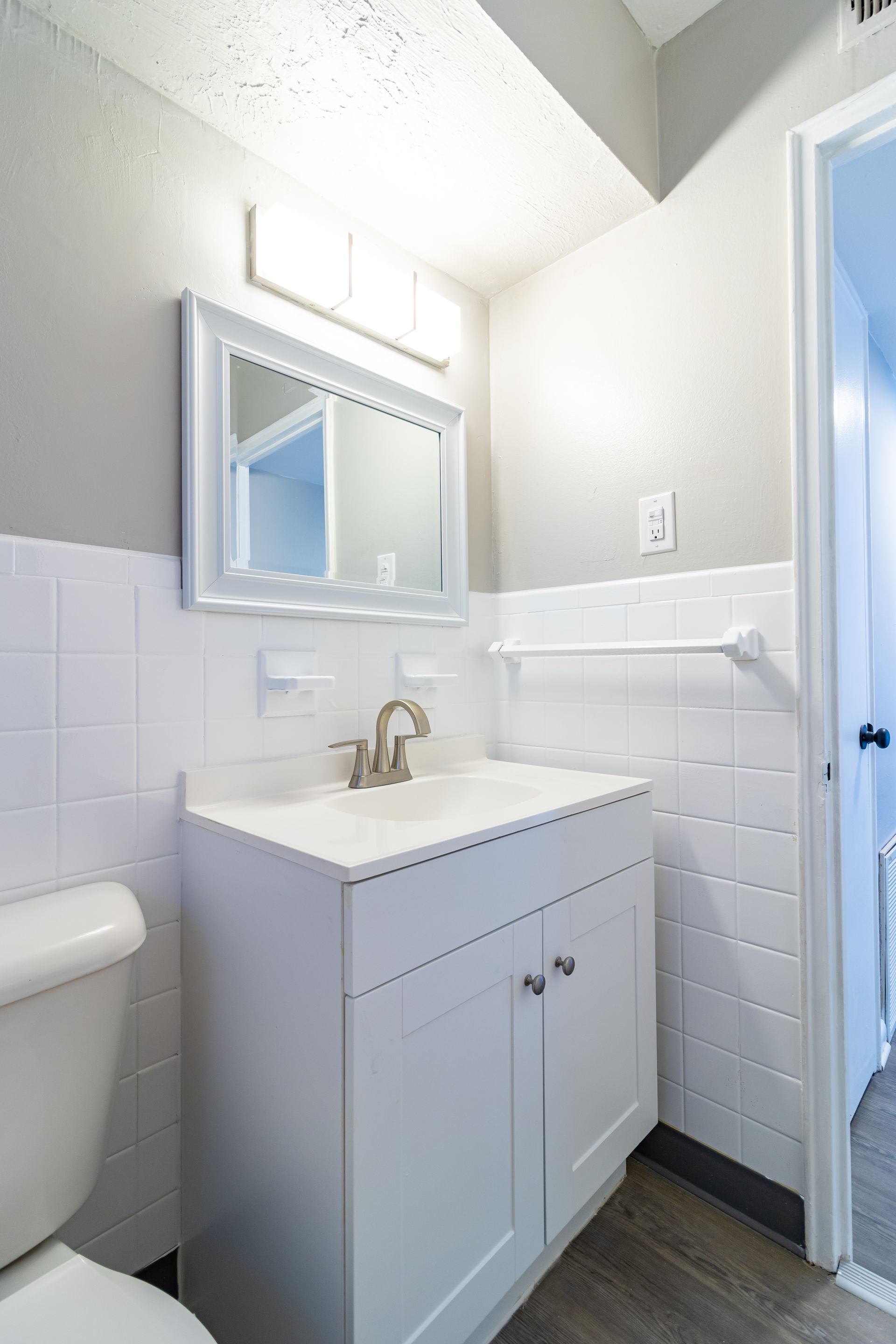 White bathroom with vanity, toilet, mirror, and door.