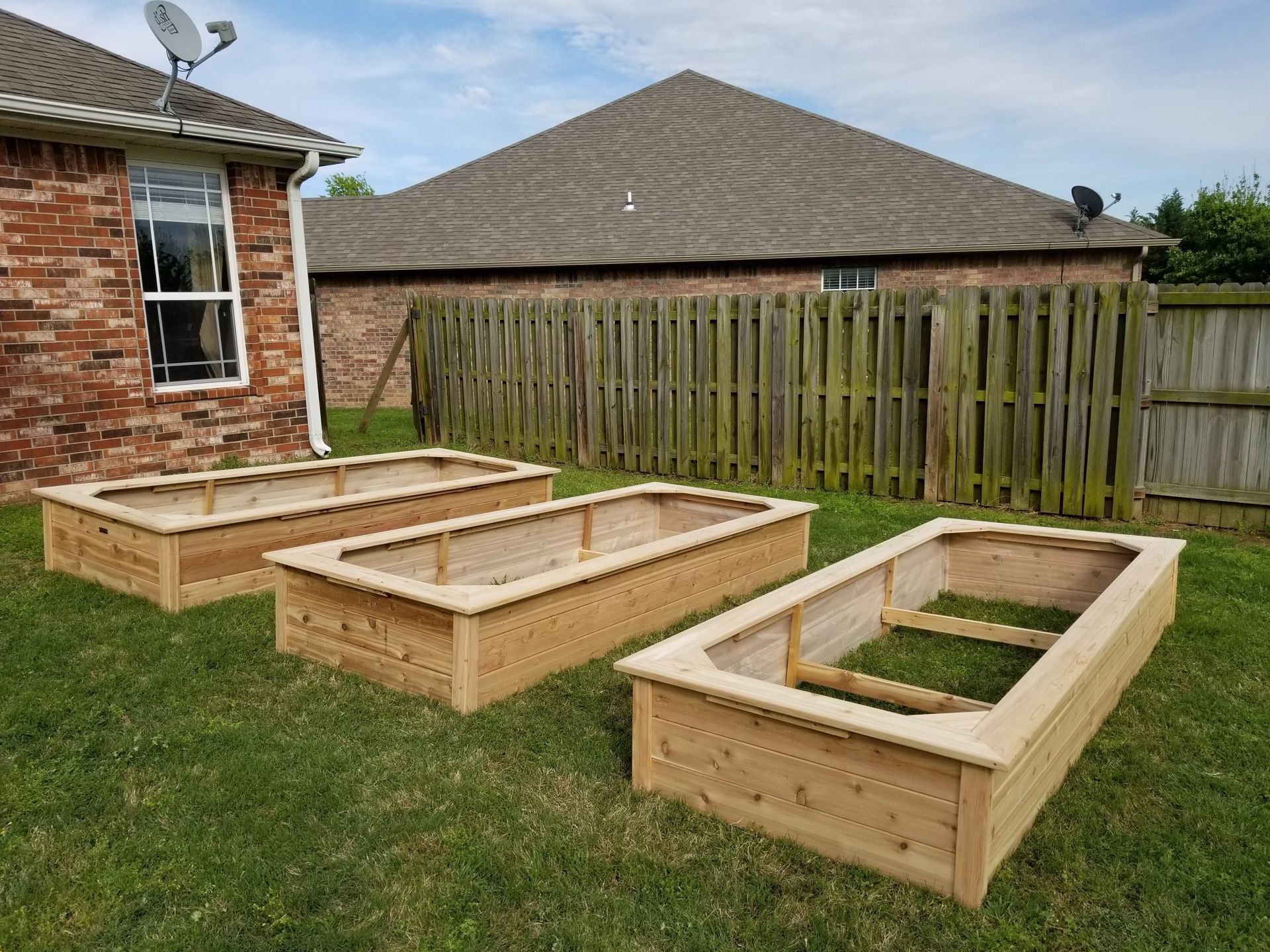 Three wooden raised garden beds are sitting in the grass in front of a house.