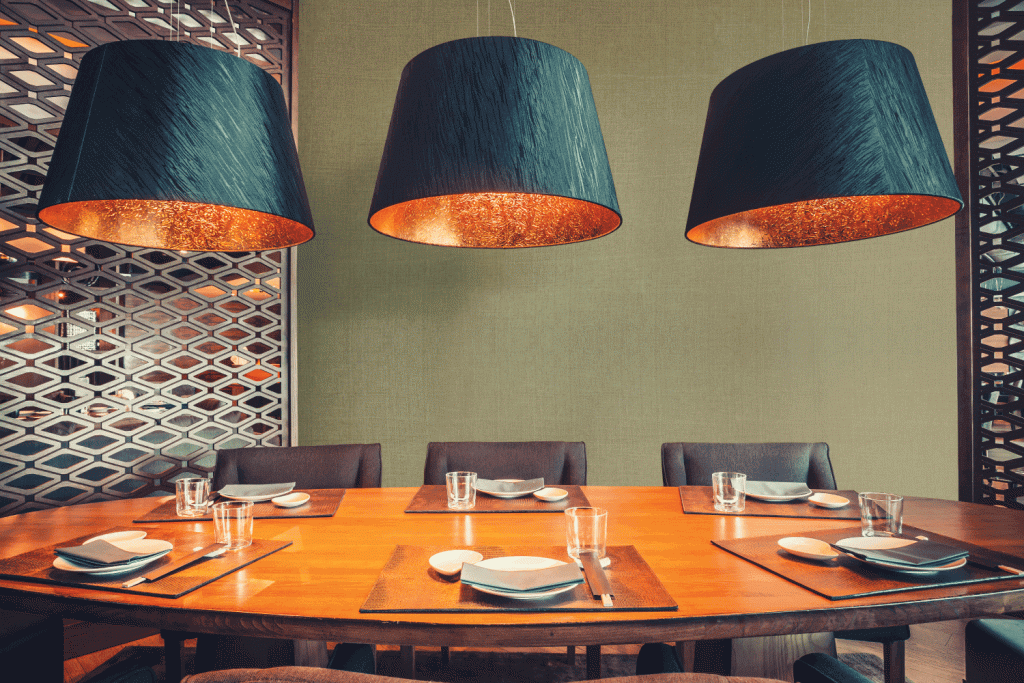 A dining room with a table and chairs and three lamps hanging from the ceiling.
