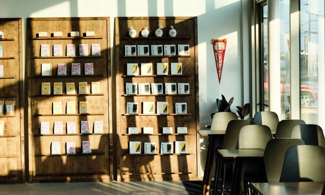 Sunlit cafe interior with wall-mounted shelves of displayed items and tables by large windows