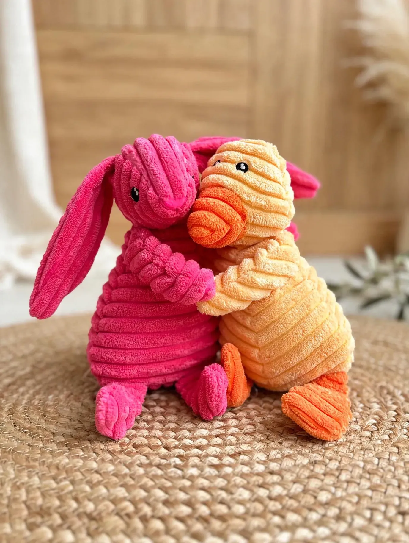 Dos animales de juguete tejidos a mano, uno rosa y otro naranja, abrazados sobre una alfombra tejida.