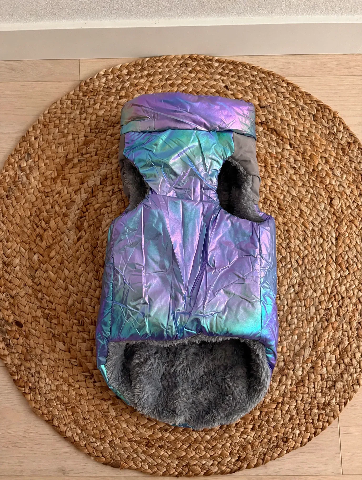 Chaleco iridiscente morado para mascotas con forro gris sobre una alfombra redonda tejida.