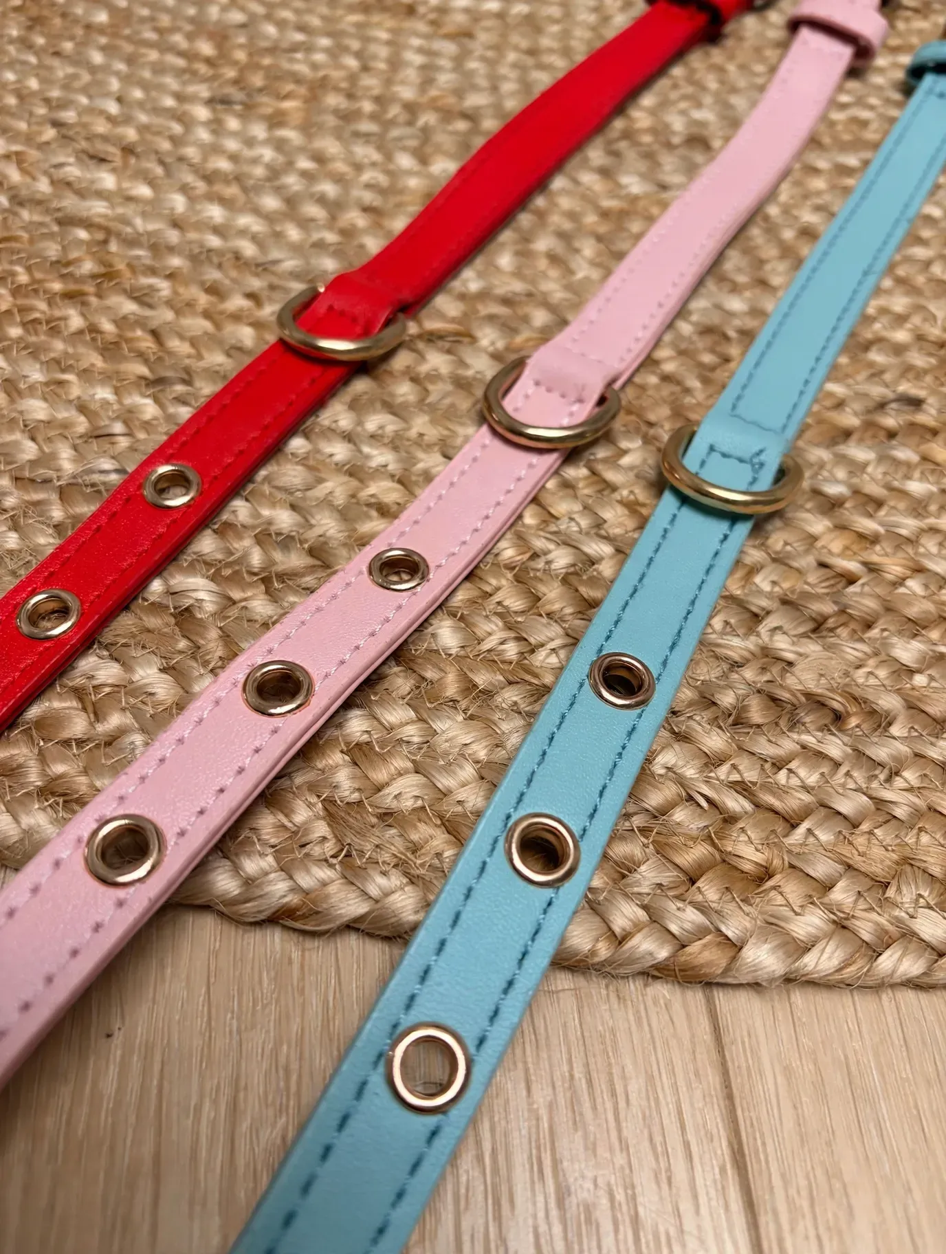 Tres collares para mascotas de colores pastel —rojo, rosa y azul— yacían uno al lado del otro sobre una estera tejida.
