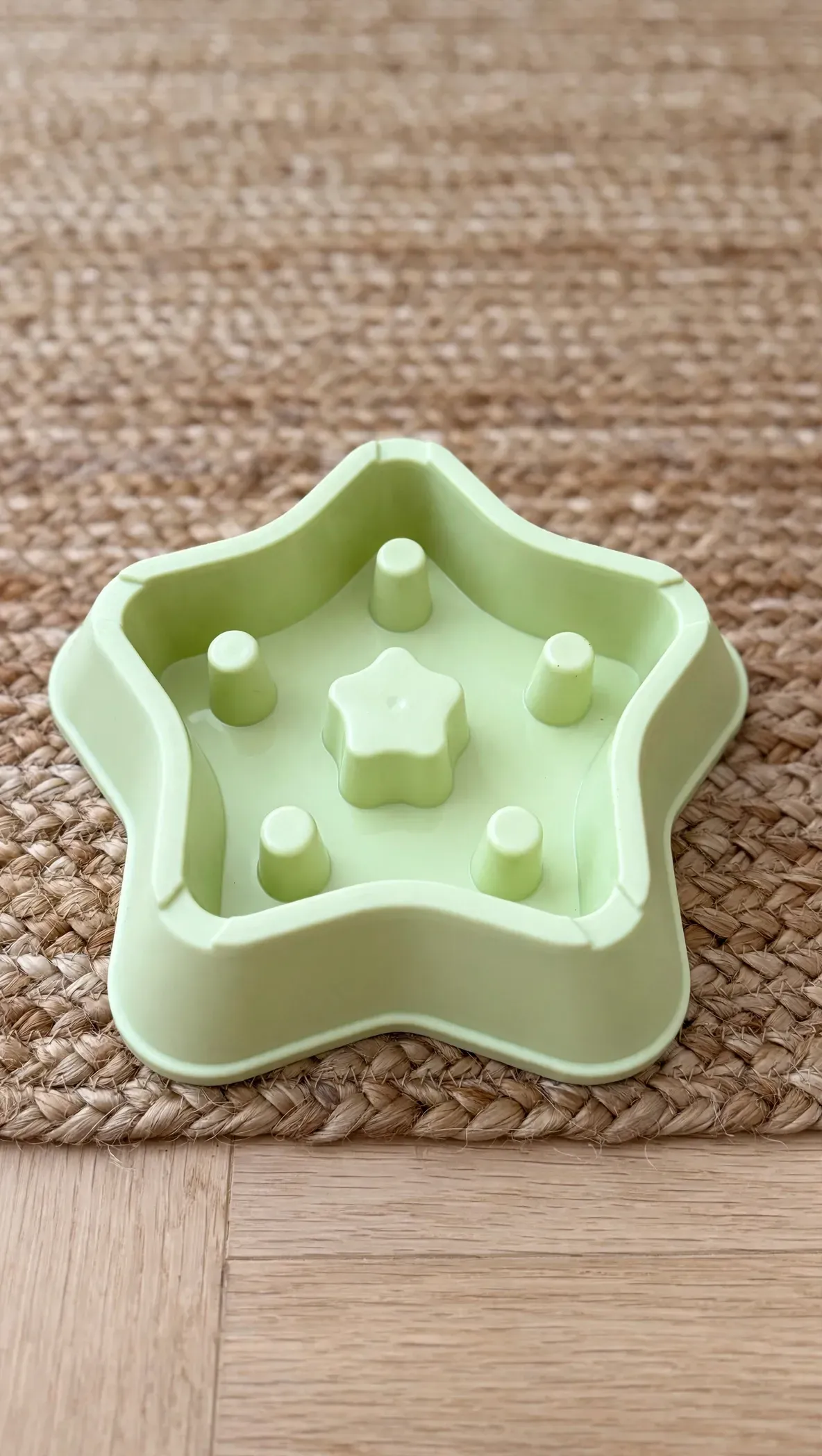 Juguete de plástico verde claro con forma de estrella y pequeñas clavijas en relieve sobre una alfombra tejida.