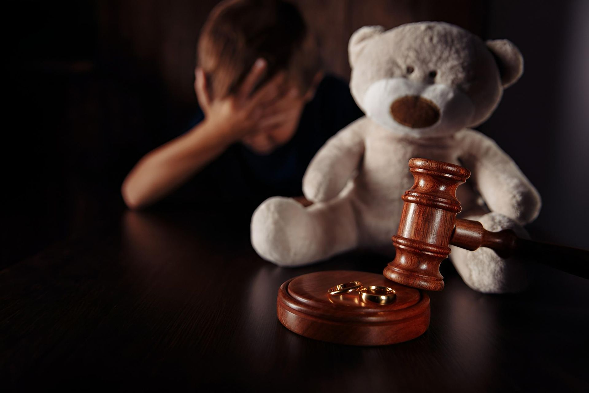 Teddy bear beside a gavel and coins, with a child covering their face in the dark background - Warland Solicitors & Conveyancing