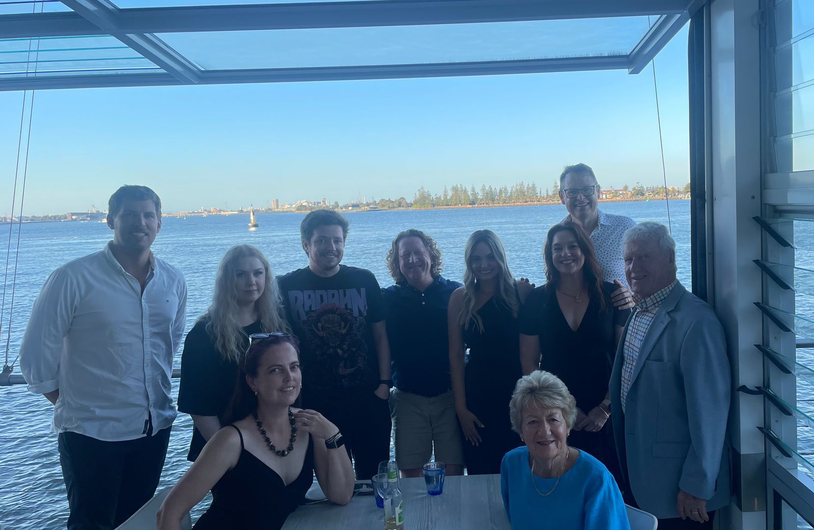 Group posing on a covered patio with waterfront view at sunset - Warland Solicitors & Conveyancing