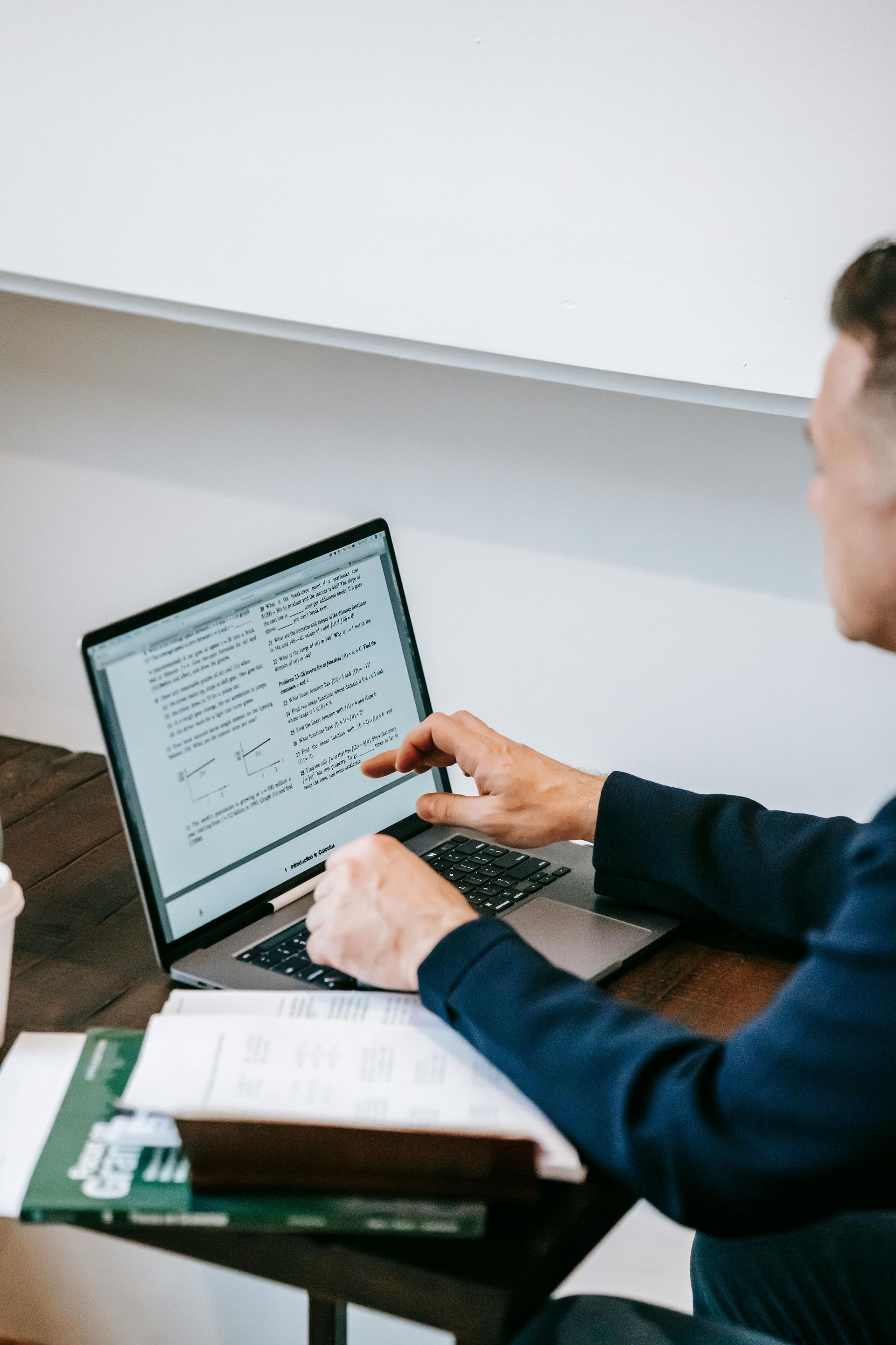 Person typing on a laptop at a desk with papers and a book nearby.