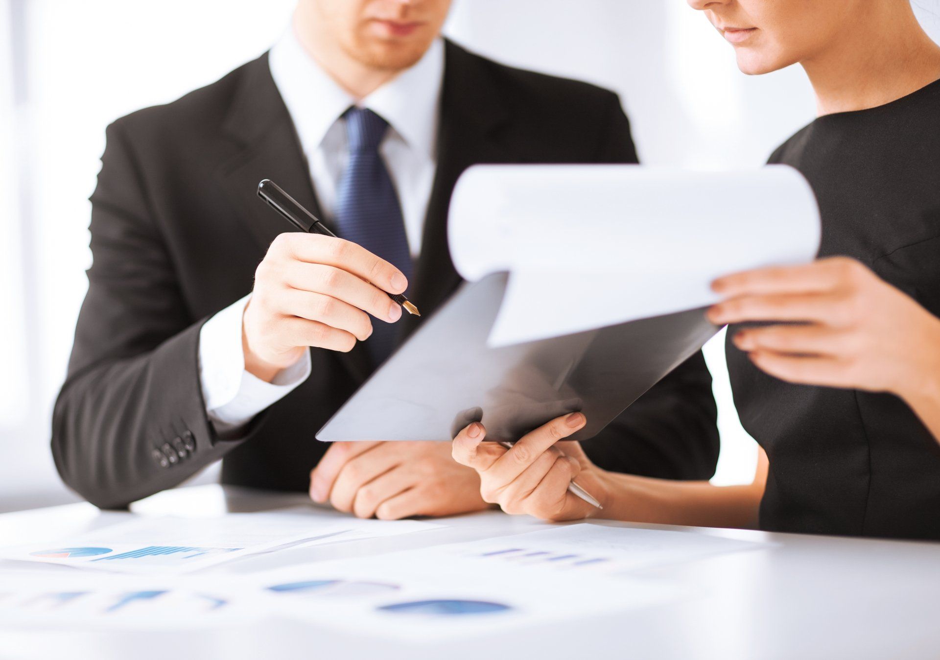 Two business professionals reviewing documents at a desk, one pointing with a pen.