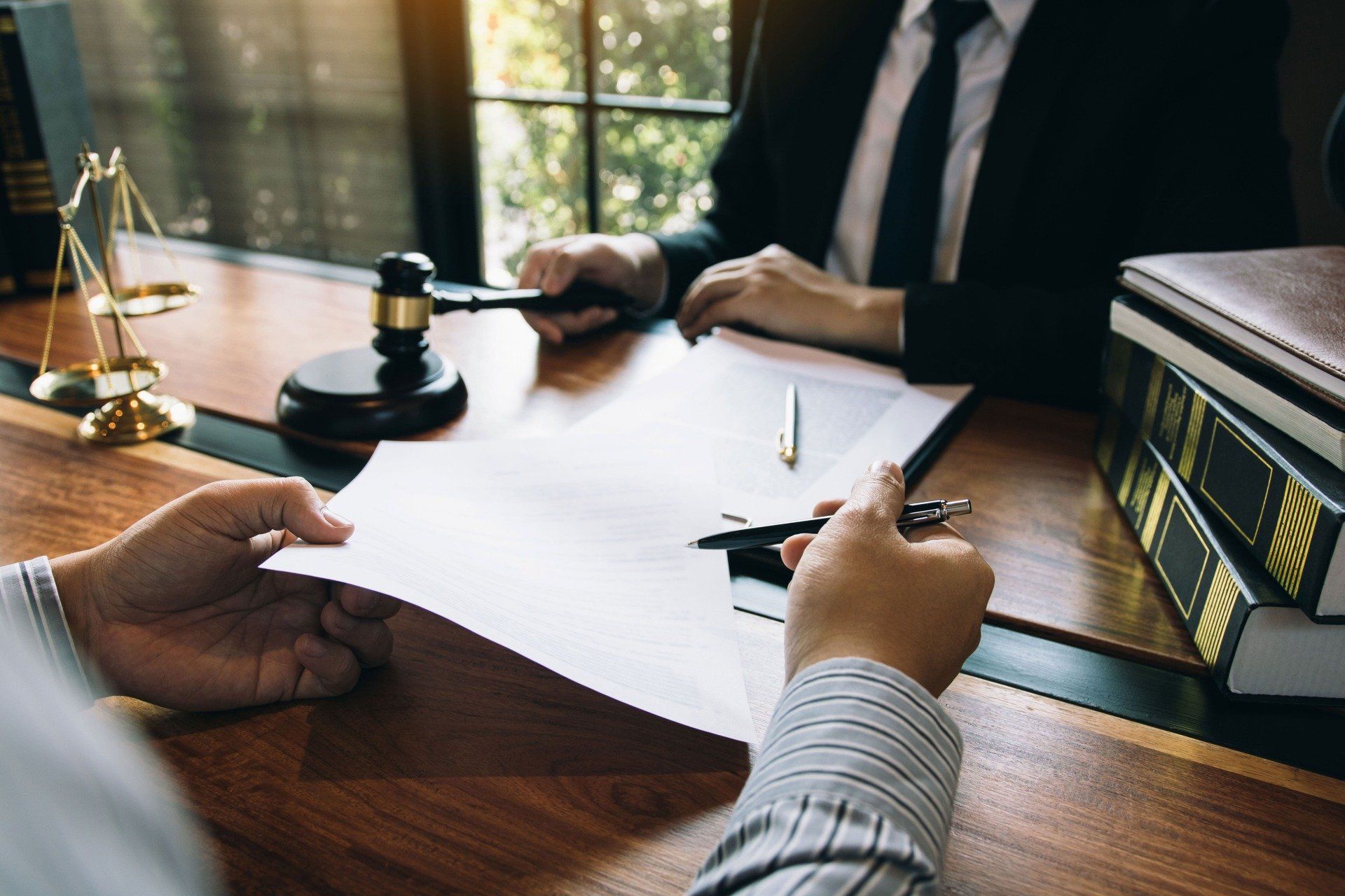 Lawyer signing a document at a desk beside a gavel and scales of justice