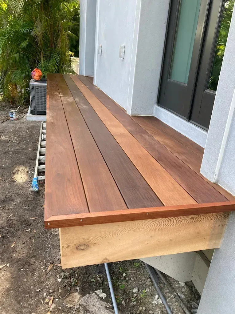 Wooden front porch deck with steps and a sliding glass door beside a white house.