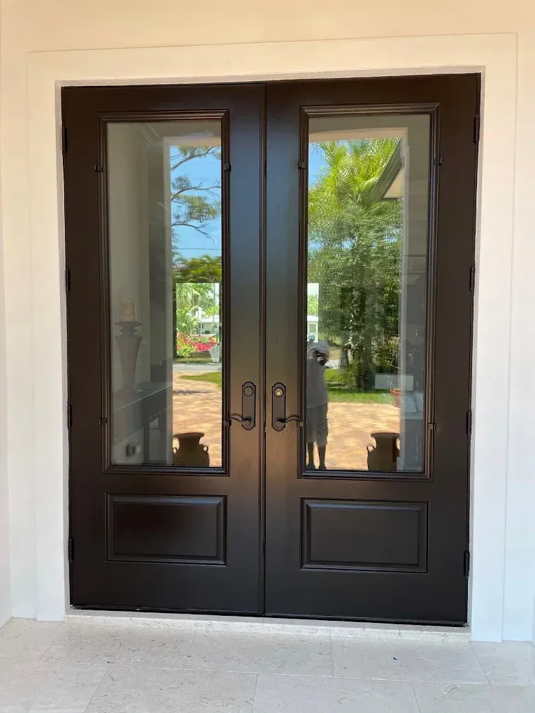 Black double glass doors with metal handles, reflecting trees outside.