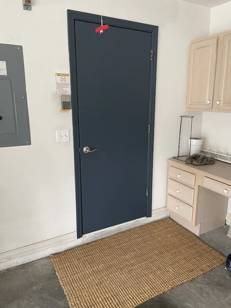 Blue door beside sink and cabinets in a small room, with woven rug on the floor.