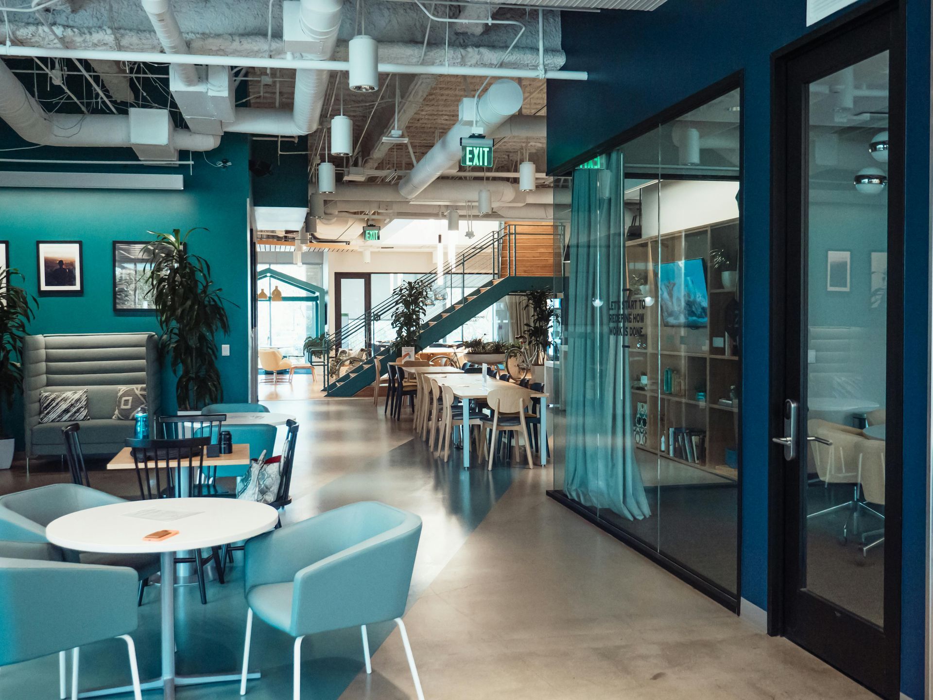 Modern cafe interior with teal chairs, white tables, and glass-walled meeting rooms