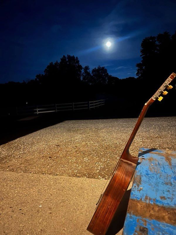 Guitar leaning on blue surface under a full moon in a dark night setting.