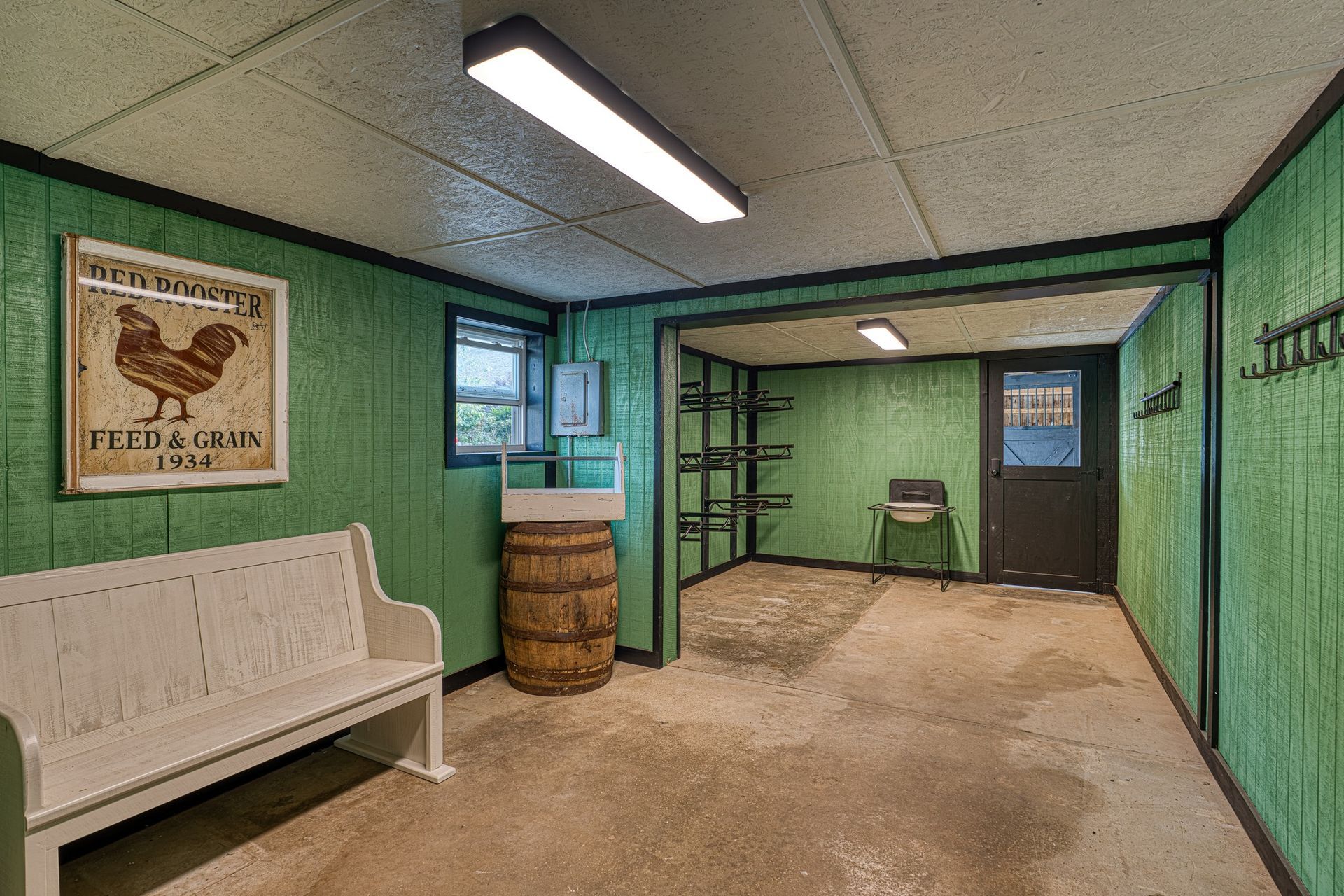 A green-paneled utility room with a bench, barrel, and shelves leading to a door.