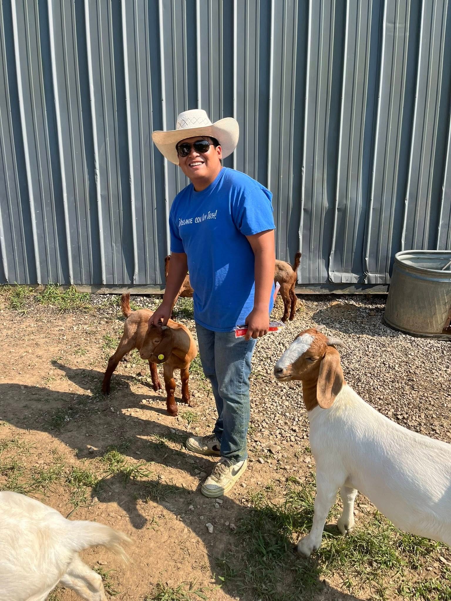 Person in cowboy hat with goats on a farm.