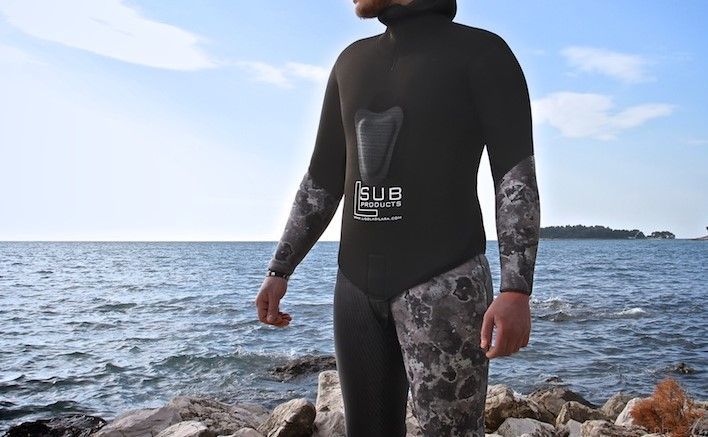 Un uomo con una muta è in piedi su una roccia vicino all'oceano.