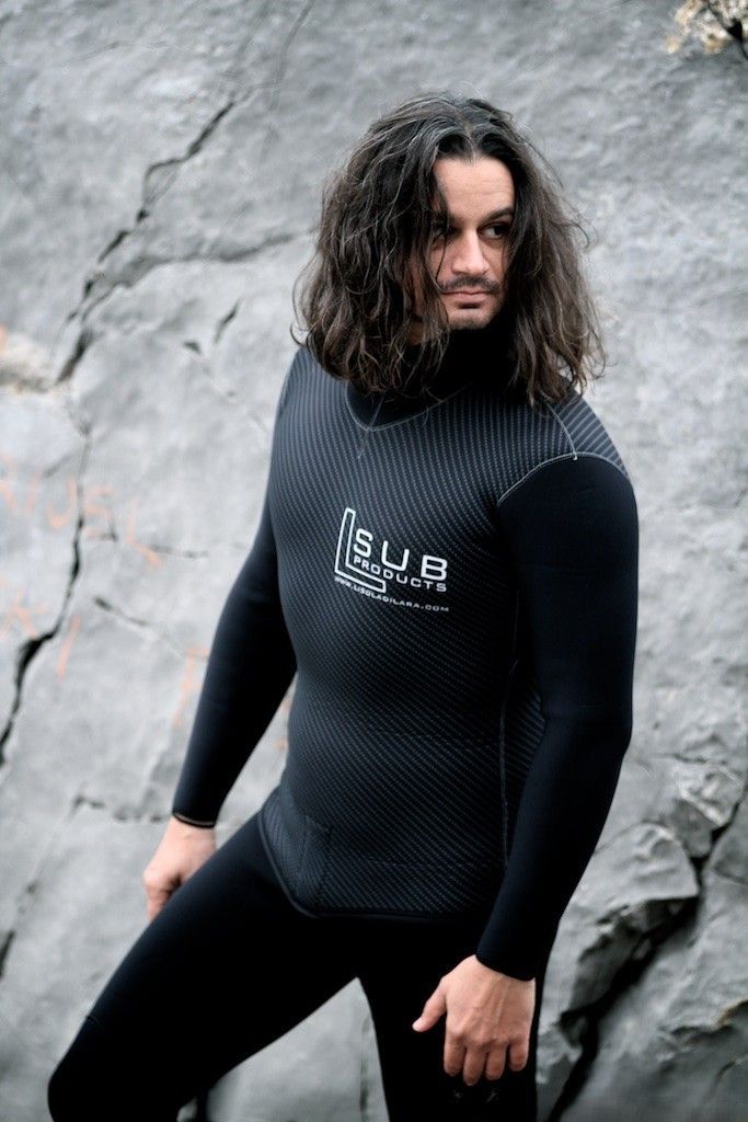 Un uomo con i capelli lunghi indossa una muta ed è in piedi su una roccia.