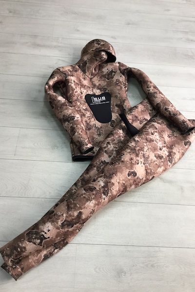 Una giacca mimetica e dei pantaloni sono stesi su un pavimento di legno.