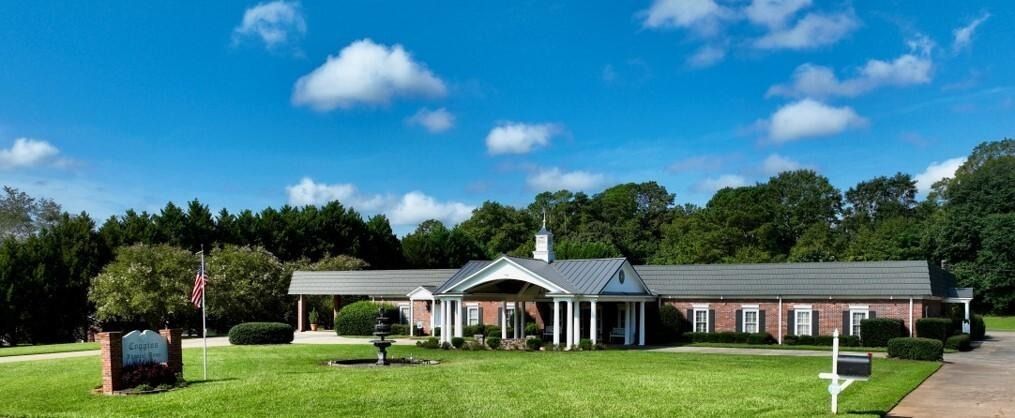 Single-story brick building with a white portico on a green lawn under a blue sky