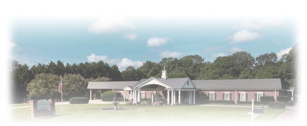 Single-story brick building with white trim and a central porch, surrounded by trees under a blue sky.