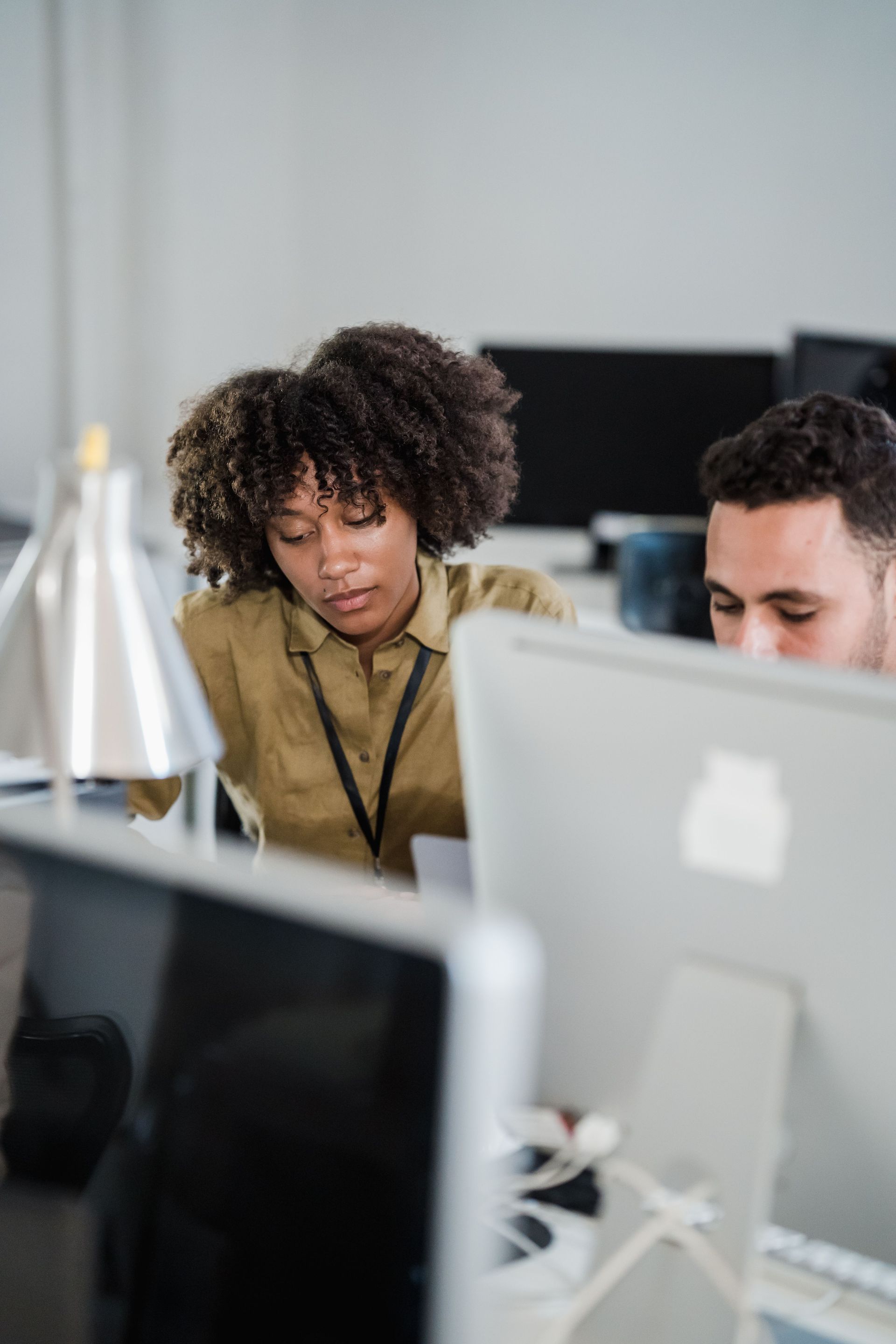 Two coworkers focused on a computer in an office, with a white monitor in the foreground.