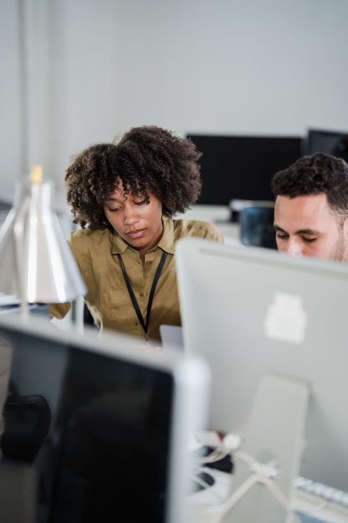 Two coworkers focused on a computer in an office, with a white monitor in the foreground.