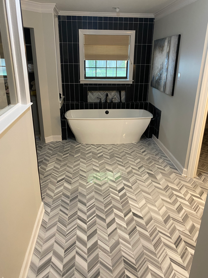 A bathroom with a bathtub and a herringbone tile floor.