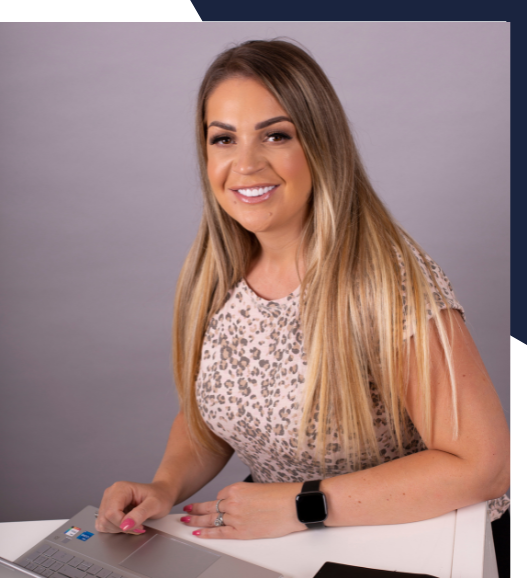A woman is smiling while sitting at a desk with a laptop
