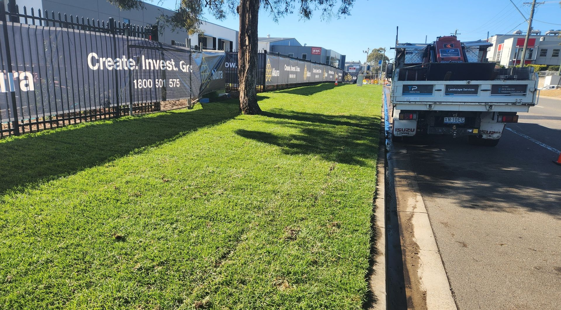 Grassy Roadside Beside A Rail Fence And Parked Utility Truck On A Sunny Street — Total Perfection In Kariong, NSW